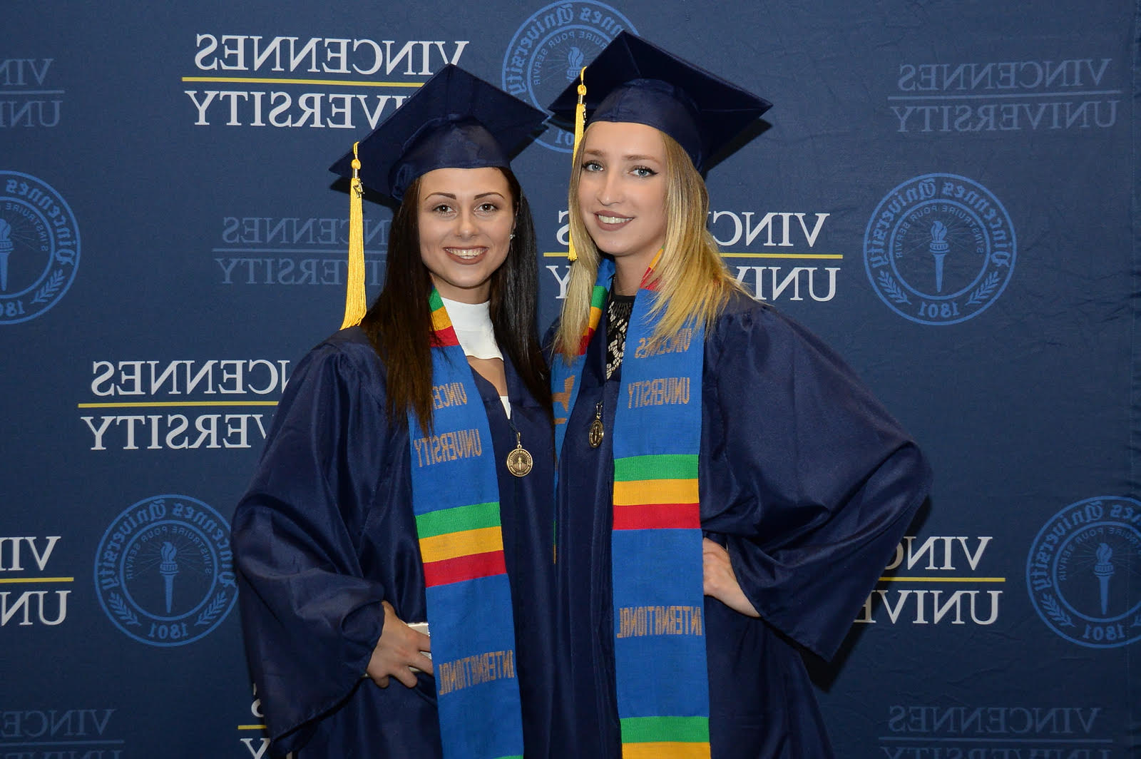 Two young ladies one blonde and one brunette smile for the photographer at graduation